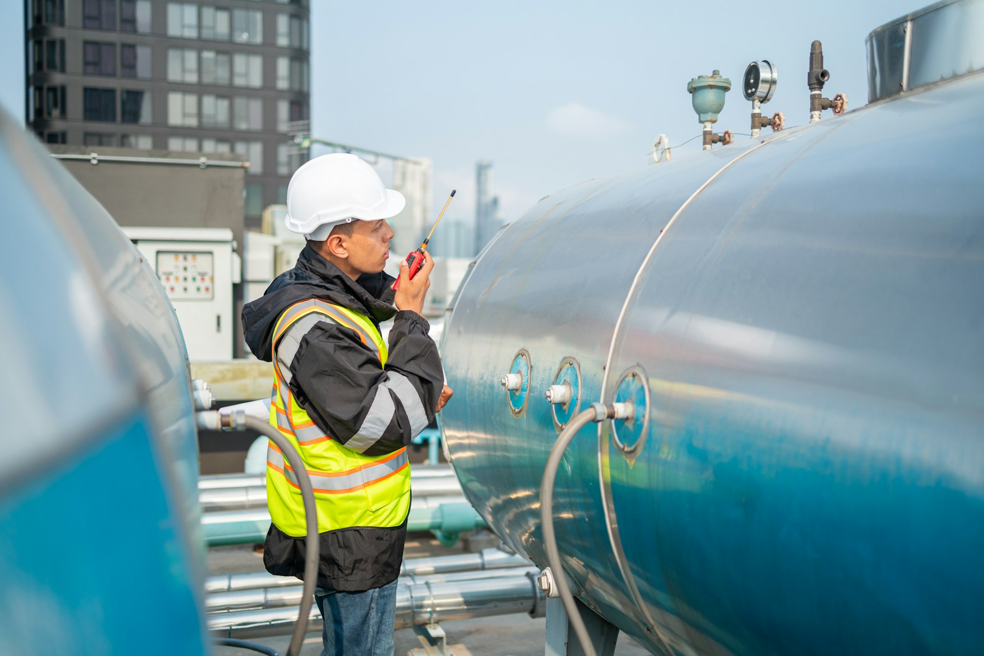Engineer inspects water heater pump system and hot water tank on industrial roof