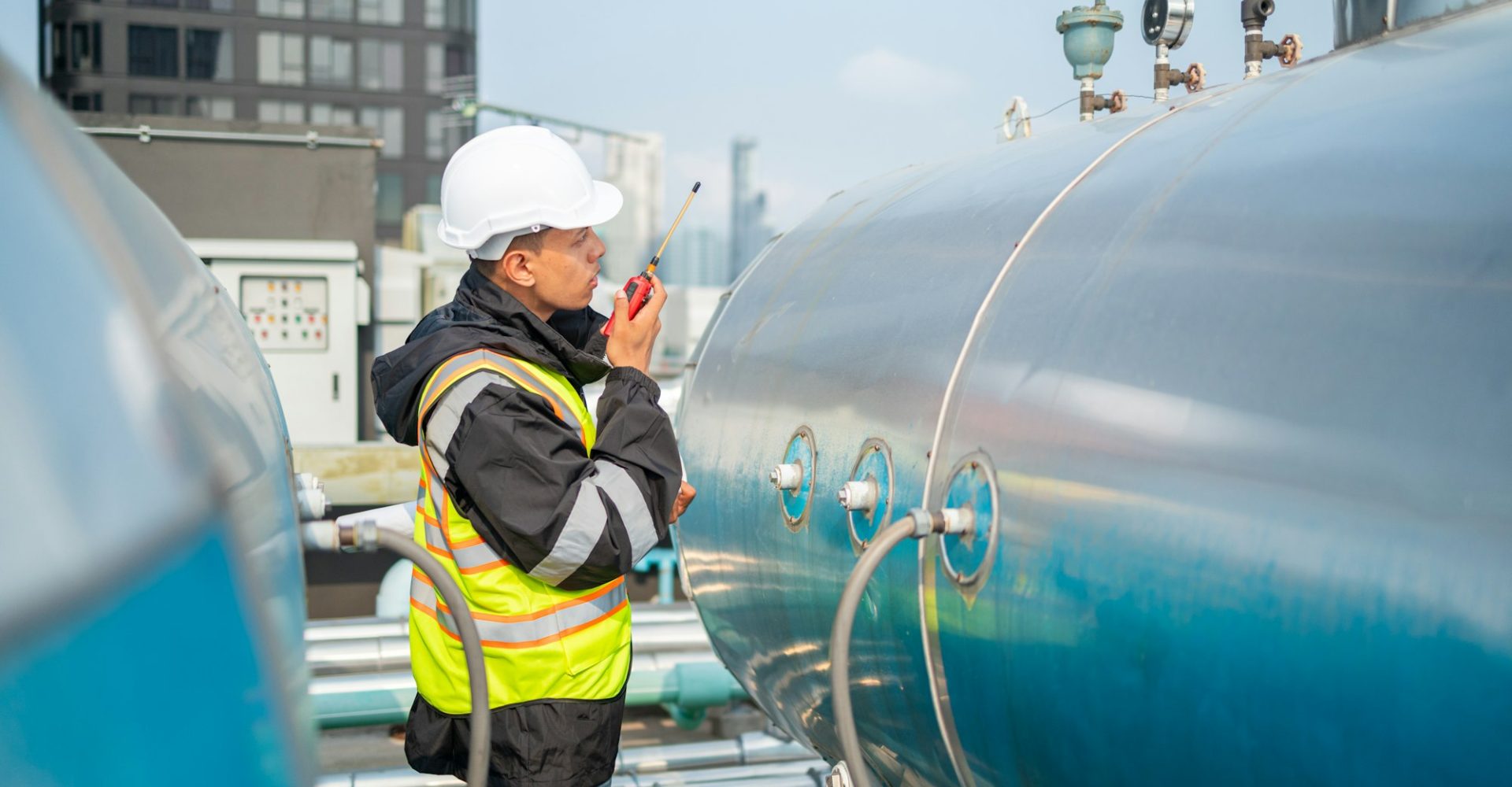 Engineer inspects water heater pump system and hot water tank on industrial roof